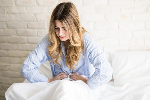 Close up of a woman gripping her stomach in pain