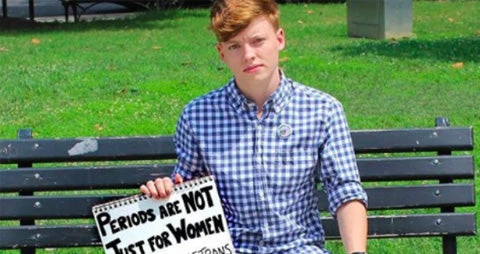 Cropped photo of a transgender male artist holding a sign saying: Periods Are Not Just For Women