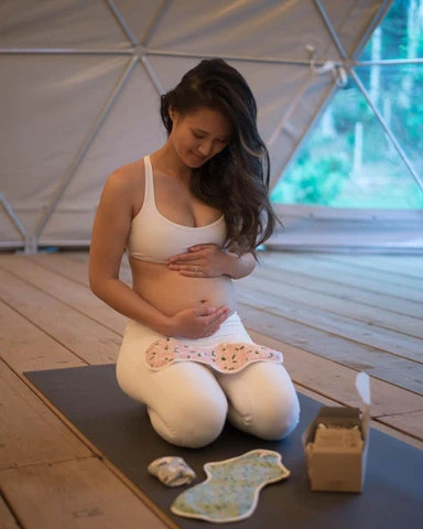 A pregnant Cam Lee kneeling on a yoga mat next to her hannahpads